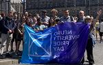 在阿姆斯特丹，一群具有里程碑意义的海外留学大学学生在户外摆姿势拍照，他们举着一面蓝色的大旗，上面写着“神经多样性骄傲日”